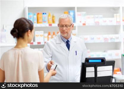 medicine, healthcare and people concept - senior apothecary taking credit card from customer at pharmacy cash register. apothecary taking customer credit card at pharmacy. apothecary taking customer credit card at pharmacy