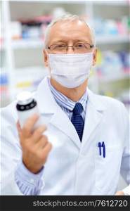 medicine, healthcare and people concept - senior apothecary wearing face protective medical mask for protection from virus disease with drug at pharmacy. old apothecary in mask with medicine at pharmacy