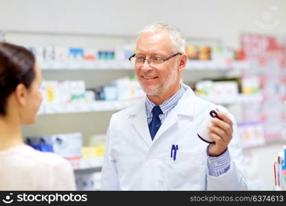 medicine, healthcare and people concept - senior apothecary with drug and female customer at pharmacy. apothecary and woman with drug at pharmacy