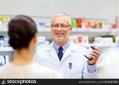 medicine, healthcare and people concept - senior apothecary with drug and female customer at pharmacy. apothecary and woman with drug at pharmacy