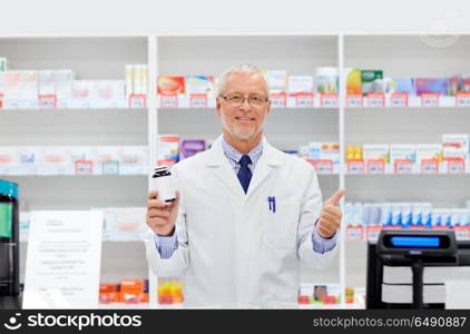 medicine, healthcare and people concept - senior apothecary with drug at pharmacy cash register showing thumbs up. senior apothecary with drug at pharmacy. senior apothecary with drug at pharmacy