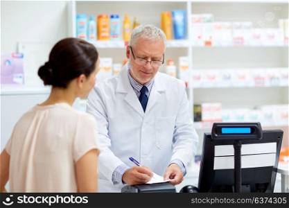 medicine, healthcare and people concept - senior apothecary writing precription for female customer at pharmacy. senior apothecary with prescription at pharmacy