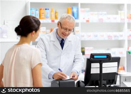 medicine, healthcare and people concept - senior apothecary writing prescription for female customer at pharmacy. senior apothecary with prescription at pharmacy. senior apothecary with prescription at pharmacy