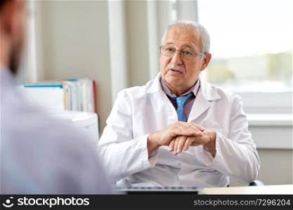 medicine, healthcare and people concept - senior doctor talking to young male patient having health problem at hospital. senior doctor talking to male patient at hospital