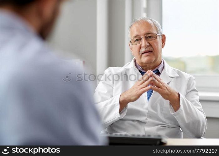 medicine, healthcare and people concept - senior doctor talking to young male patient having health problem at hospital. senior doctor talking to male patient at hospital