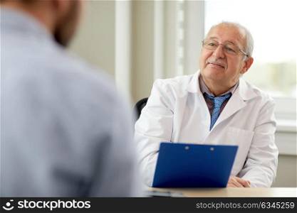 medicine, healthcare and people concept - senior doctor with clipboard talking to young male patient having health problem at hospital. senior doctor talking to male patient at hospital
