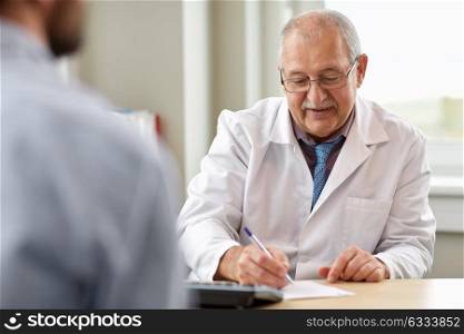medicine, healthcare and people concept - senior doctor writing prescription for young male patient at hospital. doctor writing prescription for patient at clinic
