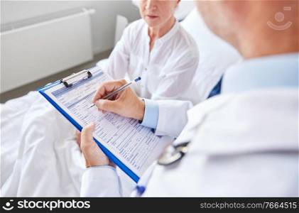 medicine, healthcare and people concept - senior woman and doctor writing to clipboard at hospital ward. senior woman and doctor with clipboard at hospital