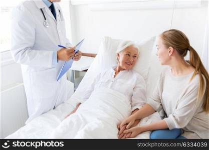 medicine, healthcare and people concept - senior woman patient with daughter and doctor with clipboard at hospital ward. senior woman and doctor with clipboard at hospital