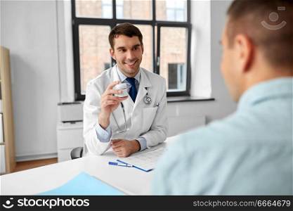 medicine, healthcare and people concept - smiling doctor showing jar with drug to male patient at medical office in hospital. doctor showing medicine to patient at hospital