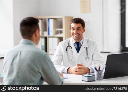 medicine, healthcare and people concept - smiling doctor talking to male patient at medical office in hospital. doctor with laptop and male patient at hospital