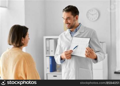 medicine, healthcare and people concept - smiling male doctor or cardiologist with clipboard showing cardiogram to woman patient at hospital. doctor showing cardiogram to woman at hospital