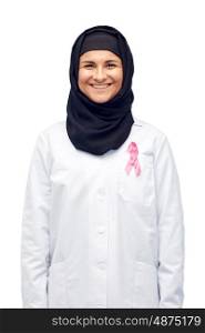 medicine, healthcare and people concept - smiling muslim female doctor wearing hijab and white coat with pink breast cancer awareness ribbon