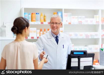 medicine, healthcare and people concept - smiling senior apothecary taking credit card from customer at pharmacy cash register. apothecary taking customer credit card at pharmacy