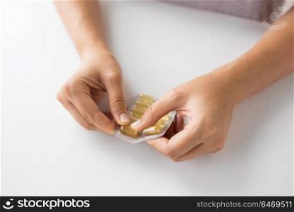 medicine, healthcare and people concept - woman hands opening pack of cod liver oil capsules. woman hands opening pack of medicine capsules