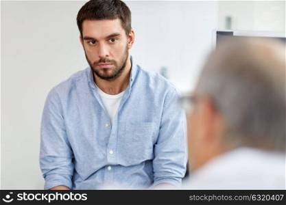 medicine, healthcare and people concept - young male patient having health problem talking to doctor at hospital. young male patient talking to doctor at hospital