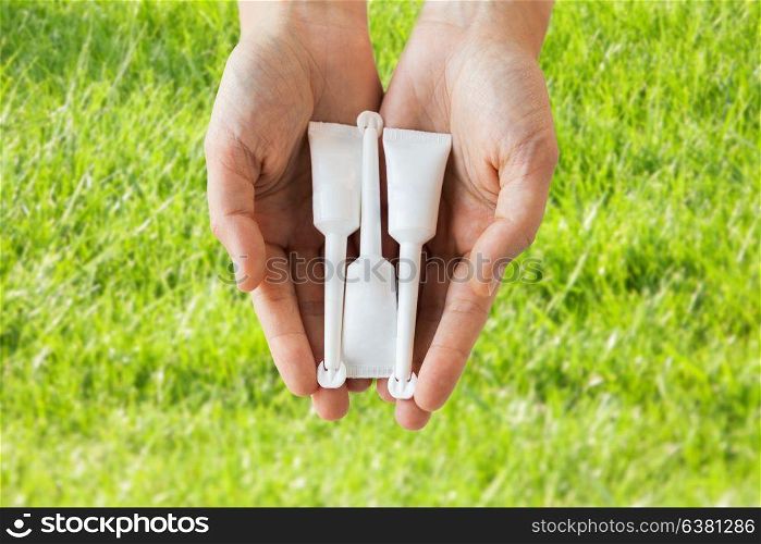 medicine, healthcare and pharmaceutics concept - hands holding tubes of micro enema over grass background. hand holding tubes of micro enema