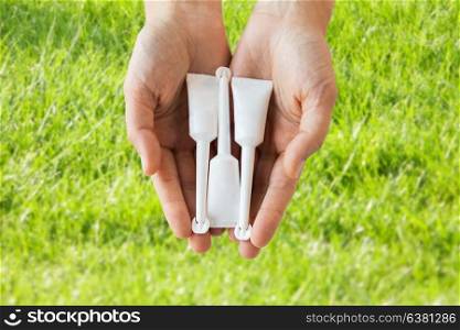 medicine, healthcare and pharmaceutics concept - hands holding tubes of micro enema over grass background. hand holding tubes of micro enema