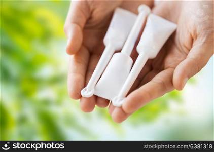 medicine, healthcare and pharmaceutics concept - hands holding tubes of micro enema over green natural background. hand holding tubes of micro enema