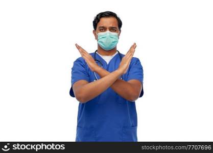 medicine, healthcare and protection concept - indian doctor or male nurse in blue uniform and protective medical mask showing refusal gesture over white background. indian male doctor mask showing refusal gesture
