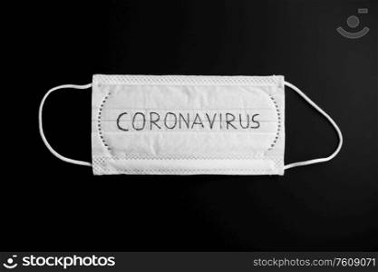 medicine, healthcare and safety concept - close up of white face protective medical mask with coronavirus word on it on black background. face protective medical mask with coronavirus