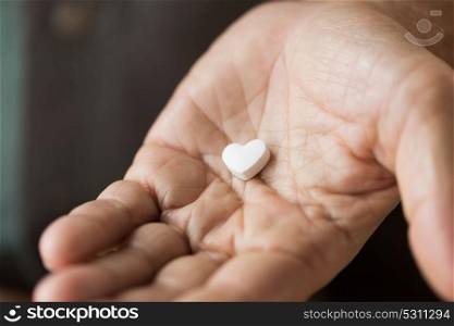 medicine, healthcare and senior people concept - close up of hand with heart shaped pill. close up of hand with heart shaped pill