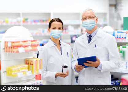 medicine, healthcare and technology concept - apothecaries wearing face protective medical mask for protection from virus disease with tablet pc computer and medication at pharmacy. apothecaries in masks with tablet pc at pharmacy