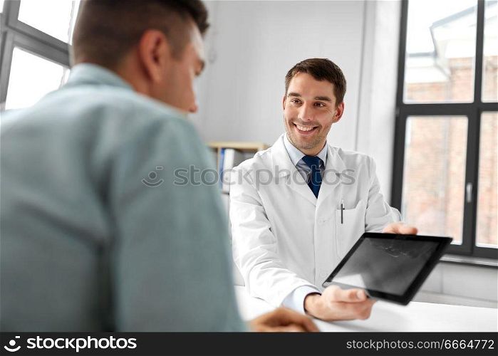 medicine, healthcare and technology concept - happy doctor with tablet pc computer and male patient talking at medical office in hospital. doctor with tablet computer and patient at clinic