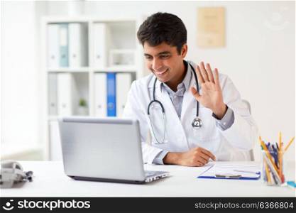 medicine, healthcare and technology concept - happy male doctor with laptop computer having video conference at clinic. doctor having video conference on laptop at clinic