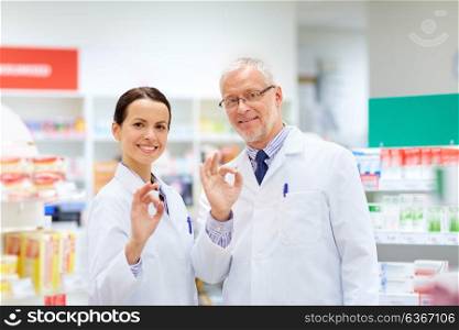 medicine, healthcare and technology concept - happy smiling apothecaries at pharmacy showing ok hand sign. apothecaries at pharmacy showing ok hand sign
