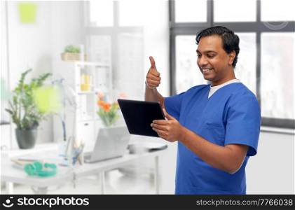 medicine, healthcare and technology concept - happy smiling doctor or male nurse having video call on tablet pc computer and showing thumbs up over medical office at hospital background. doctor or male nurse has video call on tablet pc
