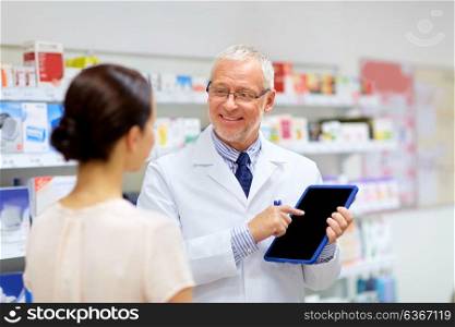 medicine, healthcare and technology concept - senior apothecary and female customer with tablet pc computer at pharmacy. apothecary and customer with tablet pc at pharmacy