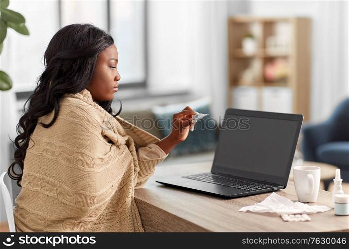 medicine, healthcare and technology concept - sick young african american woman having video call or online consultation on laptop computer and measuring temperature with thermometer at home. sick woman having video call on laptop at home