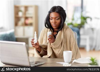 medicine, healthcare and technology concept - sick young african american woman having video call or online consultation on laptop computer at home showing drugs and sneezing. sick woman having video call on laptop at home