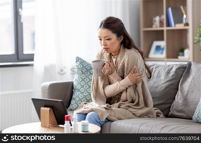 medicine, healthcare and technology concept - sick young asian woman having video call or online consultation on tablet pc computer and drinking tea at home. sick woman having video call on tablet pc at home