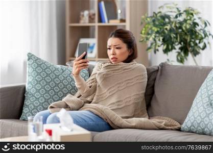medicine, healthcare and technology concept - sick young asian woman with smartphone having video call or online consultation at home. sick asian woman with smartphone at home