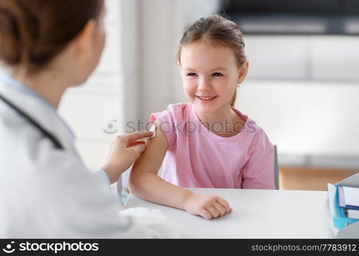 medicine, healthcare and vaccination concept - female doctor or pediatrician disinfecting arm skin of smiling little girl patient at clinic. doctor preparing girl patient for vaccination