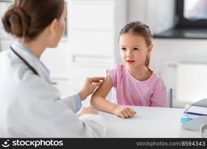 medicine, healthcare and vaccination concept - female doctor or pediatrician disinfecting arm skin of little girl patient at clinic. doctor preparing girl patient for vaccination