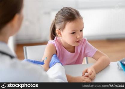medicine, healthcare and vaccination concept - female doctor or pediatrician with syringe making vaccine injection to little girl patient at clinic. doctor with syringe and girl patient at clinic