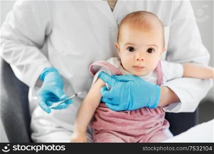 medicine, healthcare and vaccination concept - female pediatrician doctor or nurse with syringe making injection of vaccine for baby girl patient at clinic or hospital. doctor making vaccine for baby patient at clinic