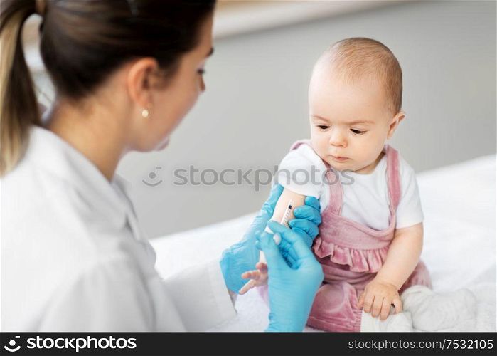 medicine, healthcare and vaccination concept - female pediatrician doctor or nurse with syringe making injection of vaccine for baby girl patient at clinic or hospital. doctor making vaccine for baby patient at clinic