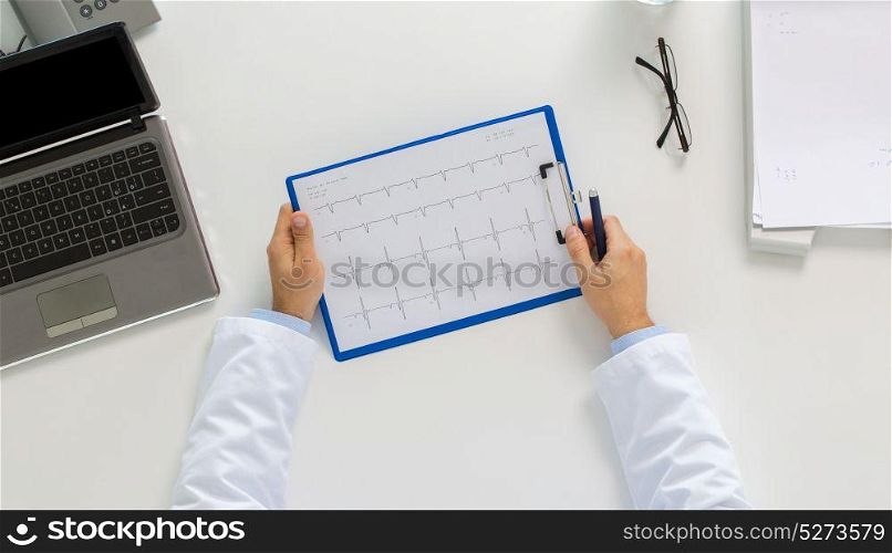 medicine, healthcare, cardiology and people concept - doctor hands with cardiogram on clipboard and laptop computer sitting at table in clinic. doctor hands with cardiogram and laptop at clinic
