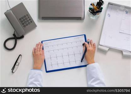 medicine, healthcare, cardiology and people concept - doctor hands with cardiogram, phone and laptop computer at table. doctor hands with cardiogram at table