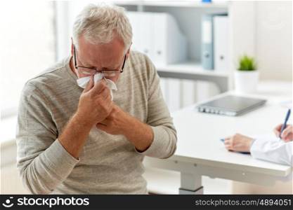 medicine, healthcare, flu and people concept - senior man blowing nose with napkin and doctor with clipboard writing at medical office at hospital
