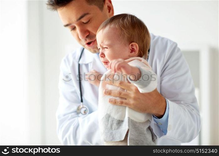 medicine, healthcare, pediatry and people concept - doctor or pediatrician holding sad crying baby girl on medical exam at clinic. doctor or pediatrician with crying baby at clinic
