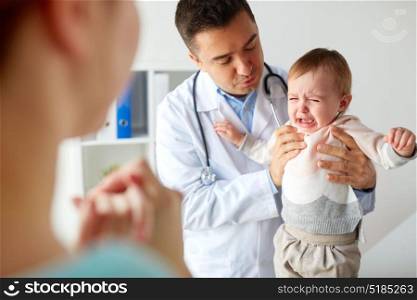 medicine, healthcare, pediatry and people concept - doctor or pediatrician holding sad crying baby girl on medical exam at clinic. doctor or pediatrician with crying baby at clinic