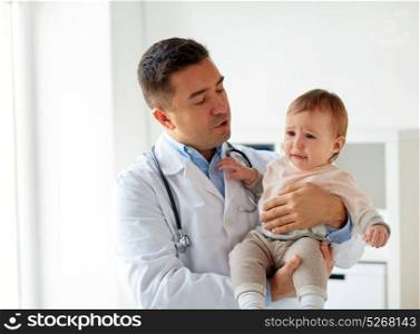 medicine, healthcare, pediatry and people concept - doctor or pediatrician holding sad crying baby girl on medical exam at clinic. doctor holding crying baby at clinic