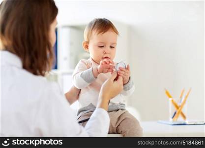 medicine, healthcare, pediatry and people concept - doctor with stethoscope listening to happy smiling baby girl on medical exam at clinic. doctor with stethoscope and happy baby at clinic