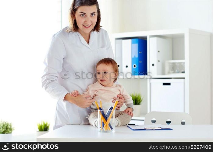 medicine, healthcare, pediatry and people concept - happy doctor or pediatrician holding baby on medical exam at clinic. happy doctor or pediatrician with baby at clinic
