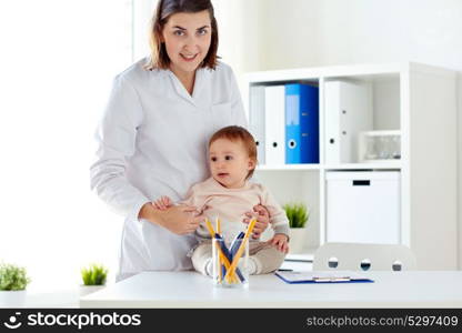 medicine, healthcare, pediatry and people concept - happy doctor or pediatrician holding baby on medical exam at clinic. happy doctor or pediatrician with baby at clinic